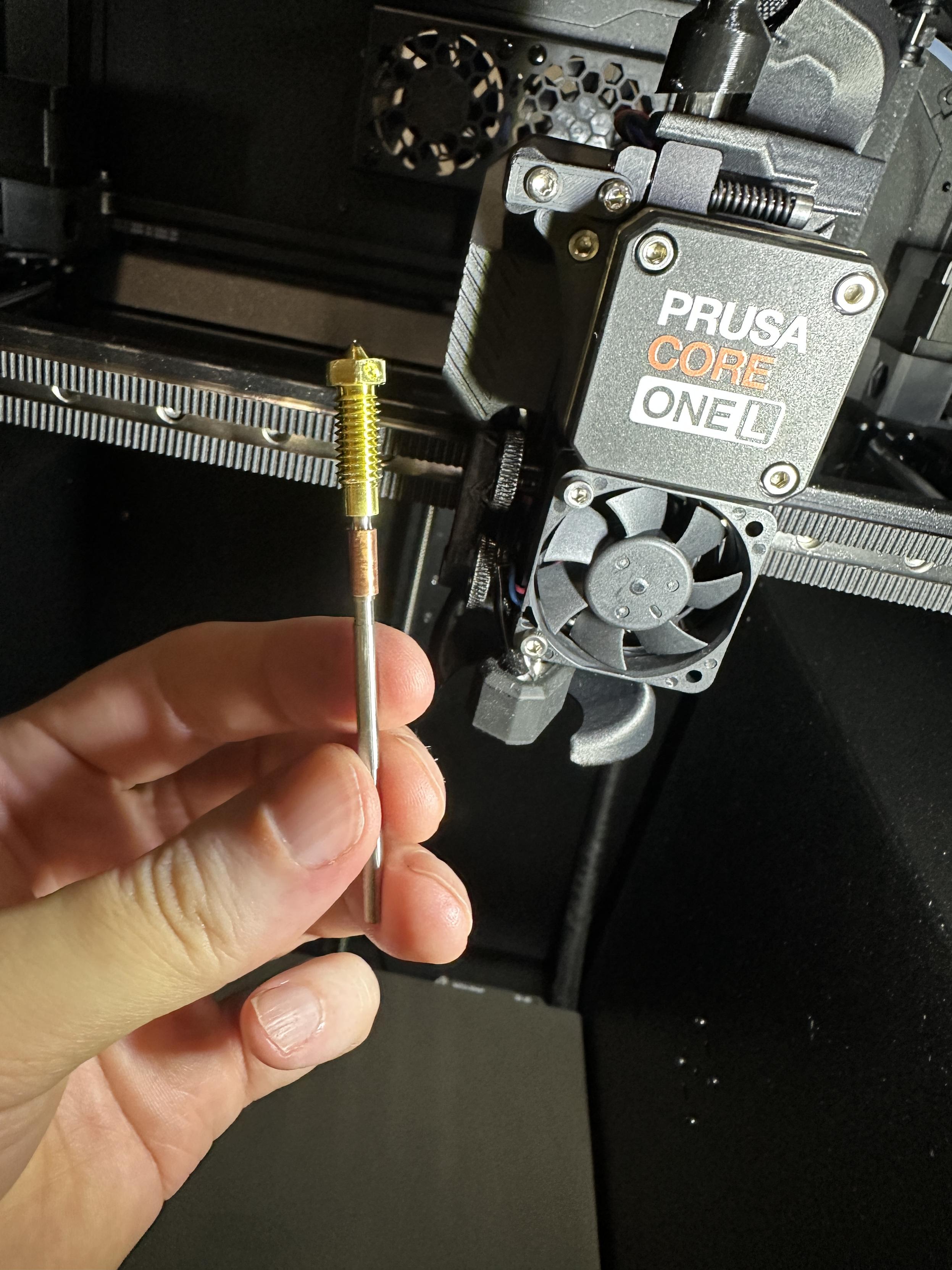 A Prusa Nextruder high flow nozzle, with Core One L in the background.